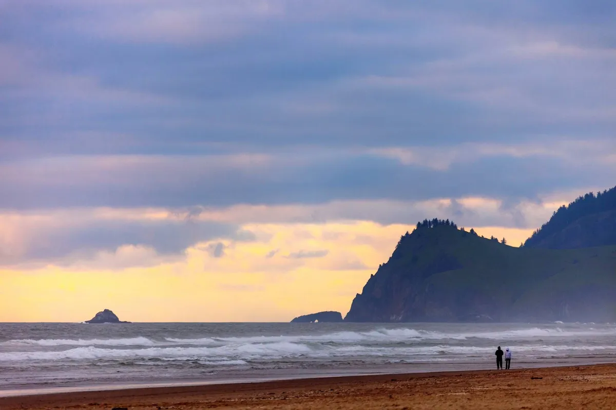 A romantic coastal scene with a couple walking along the shoreline, distant cliffs, gentle ocean waves, and the sun setting over the horizon. The tranquil atmosphere invites leisurely strolls and memorable moments by the sea.