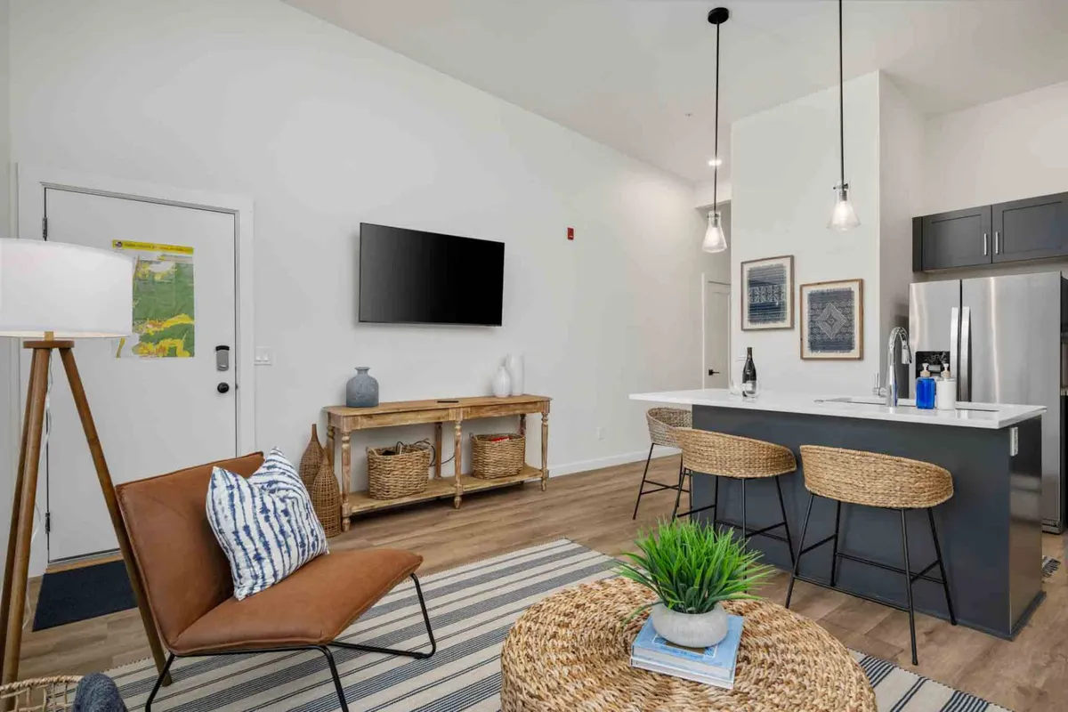 A stylish and contemporary interior featuring a comfortable armchair, kitchen island, decorative wall art, TV, and elegant lighting fixtures. The space feels both modern and welcoming, ideal for greeting guests or unwinding in solitude after leaving the city’s bustle.