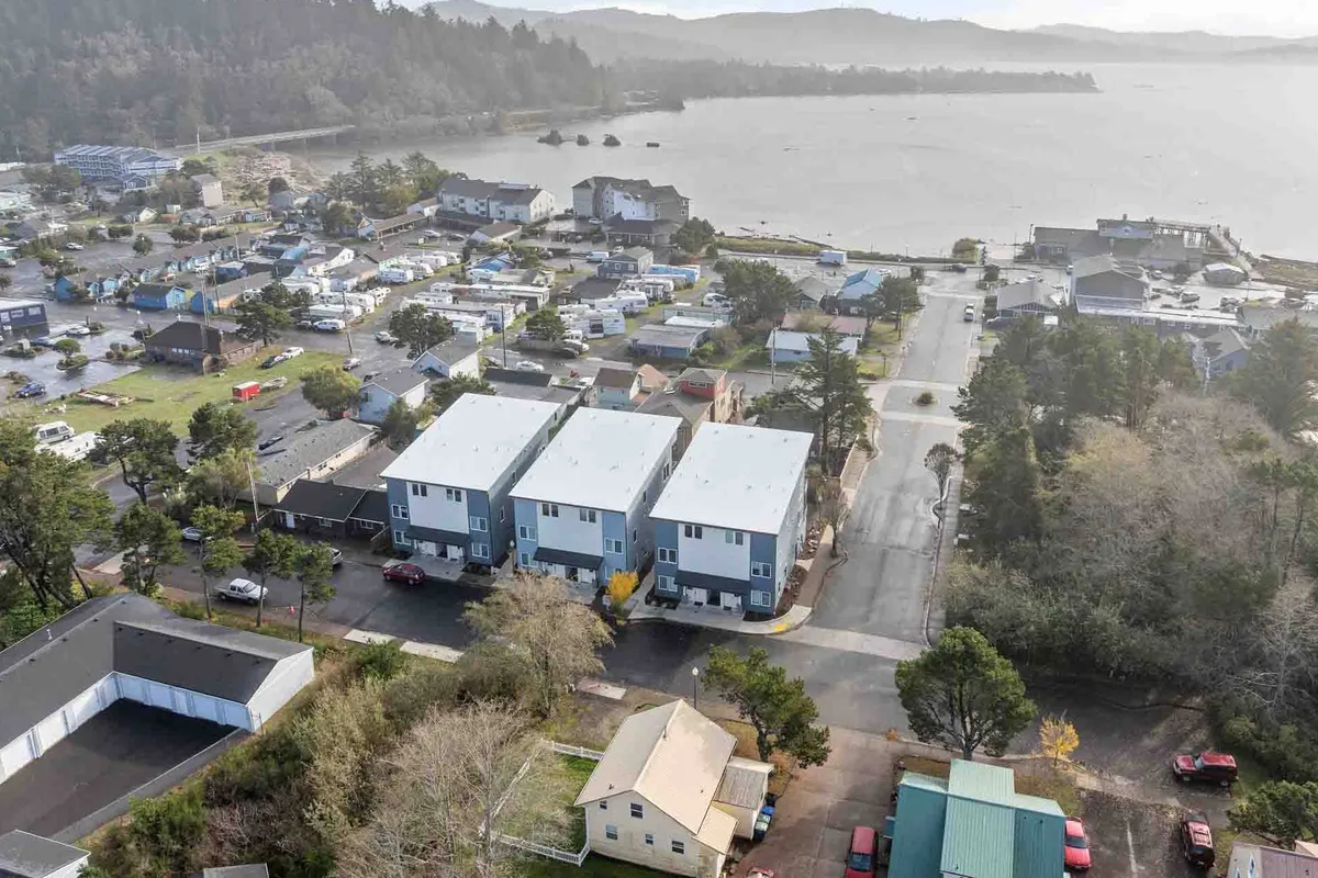 An inviting exterior shot featuring three modern residential buildings set against the waterfront, with lush greenery along the shoreline. The scene suggests easy access to water activities, community gatherings, and leisurely walks near the bay.