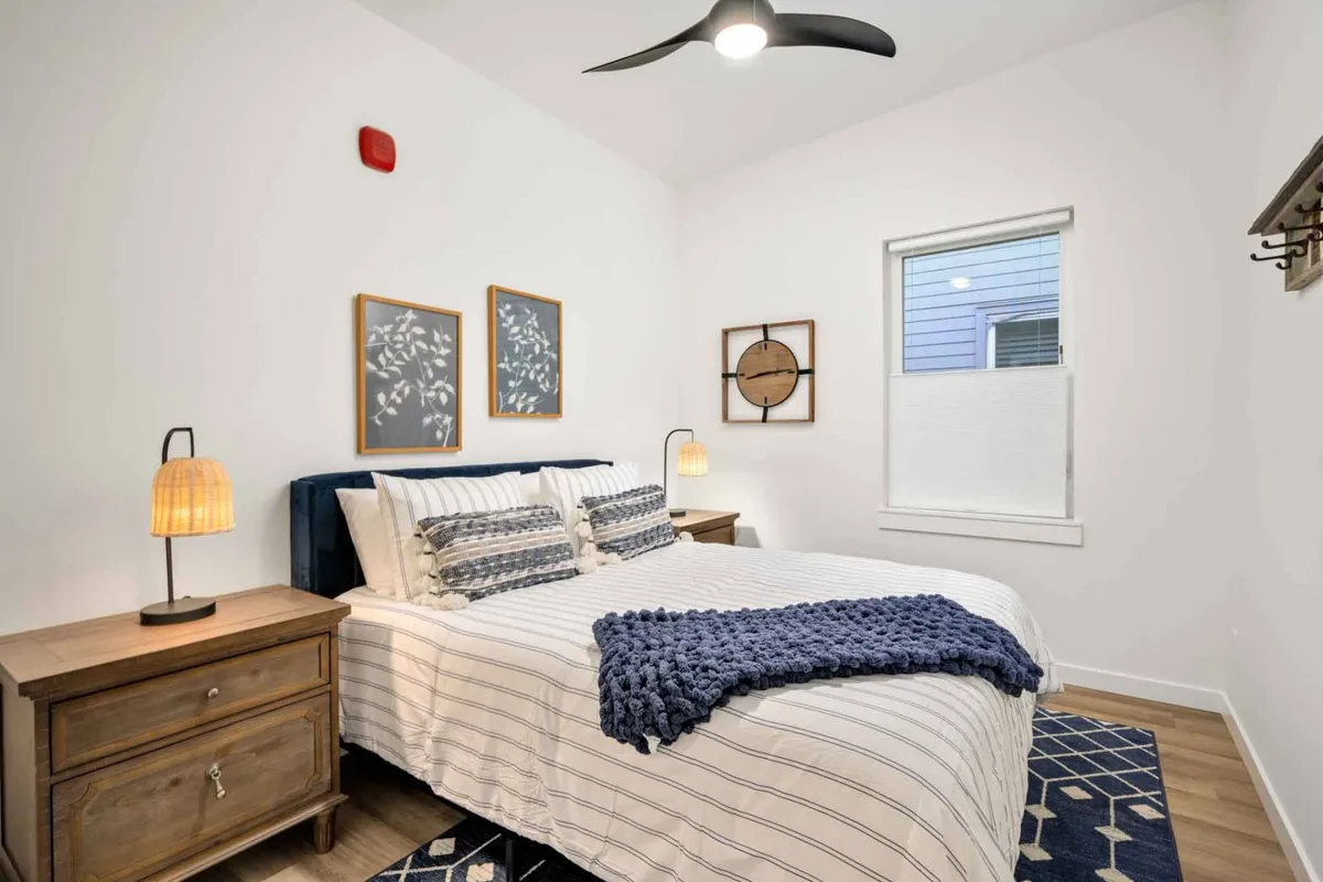 A cozy bedroom setting featuring a bed with decorative pillows, twin bedside lamps, and framed artwork. The warm lighting and soft textures create a tranquil, calming environment perfect for relaxation or unwinding with a book.