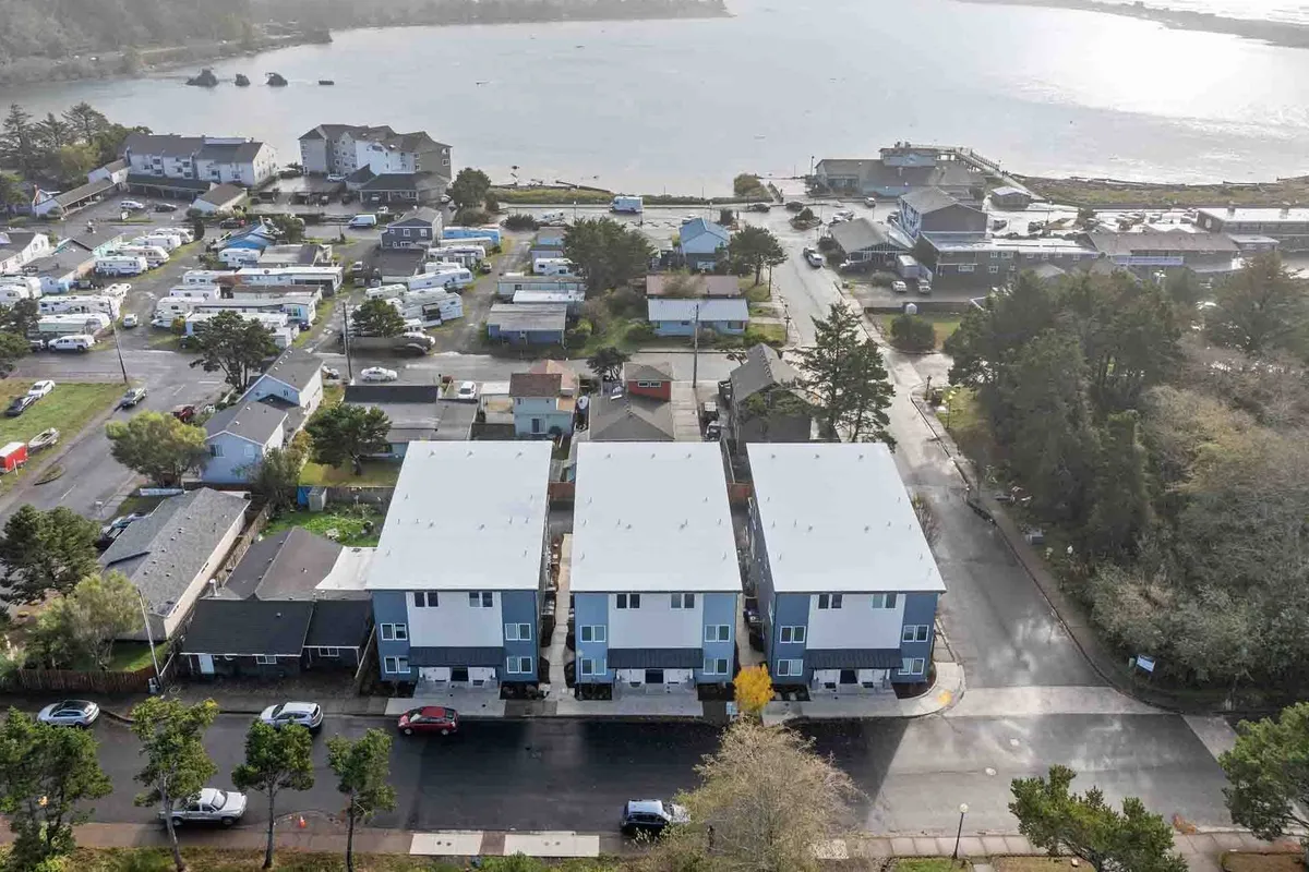 A trio of modern houses overlooks a sparkling waterfront bordered by lush greenery. The scene hints at easy access to nature trails, community spaces, and opportunities for water-based recreation.
