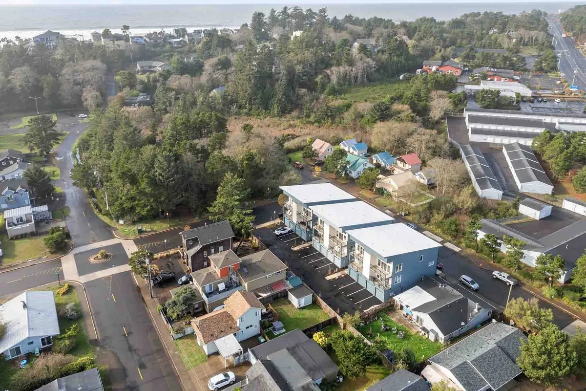 A wide exterior shot featuring a row of houses, a new apartment complex, a tree line, and distant ocean views. The visual narrative evokes community, discovery, and the excitement of finding neighborhood gems—perfect for culinary explorations.