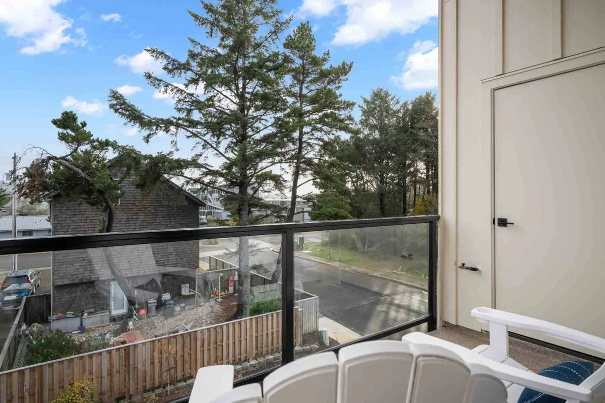 This image shows a peaceful balcony setting with a view of tall trees and neighboring houses. The balcony is designed for relaxation, with space to sit and enjoy nature, observe wildlife, or feel the gentle coastal breeze.
