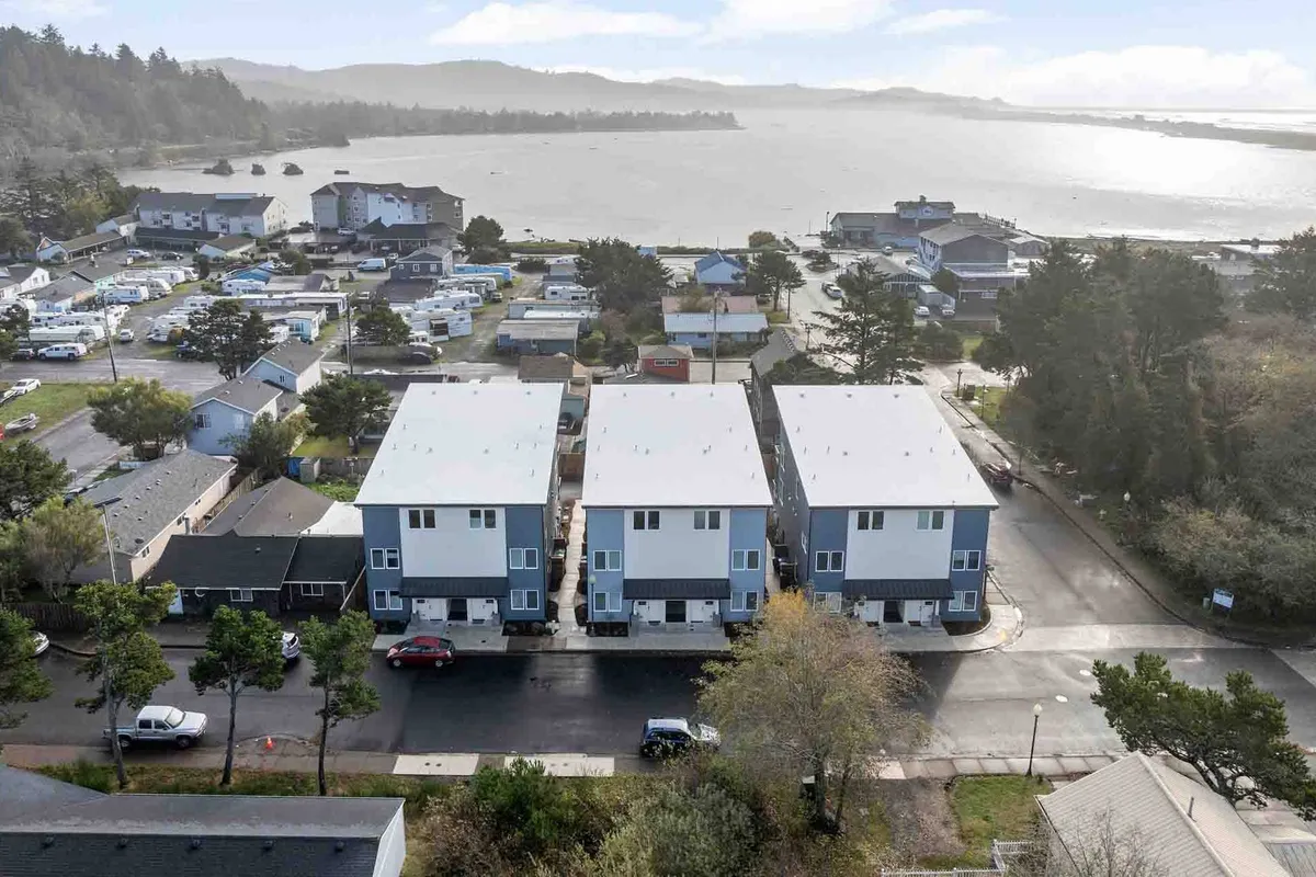 An exterior view of modern townhouses with a waterfront backdrop and lush surrounding greenery. The image subtly suggests a lifestyle where residents can enjoy outdoor activities, perhaps making their way to nearby markets or restaurants with scenic views.
